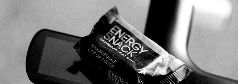 Close-up av en PurePower Energy Snack på et sykkelstyre; emballasjen i fokus som eksempel på en liten, karbohydratrik pre-workout-snack, enkel å ha med 30–60 min før intervalløp.